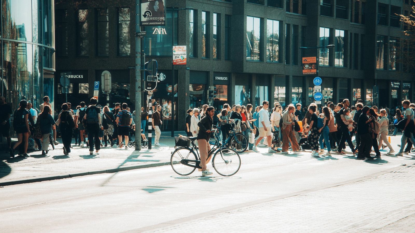 Drukke winkelstraat in Utrecht met fietsers en voetgangers op een zonnige dag
