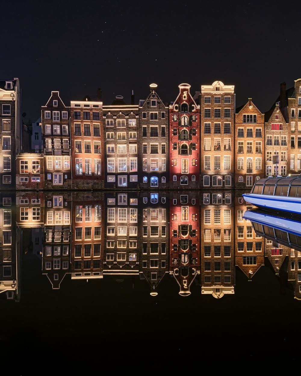 Verlichte grachtenpanden bij nacht, met reflectie in het water